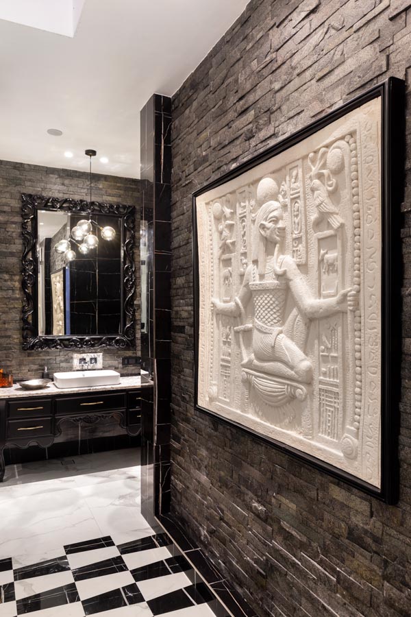 A Egyptian inspired wall mural at the entrance of a bathroom with black and white tiles - Beautiful Homes