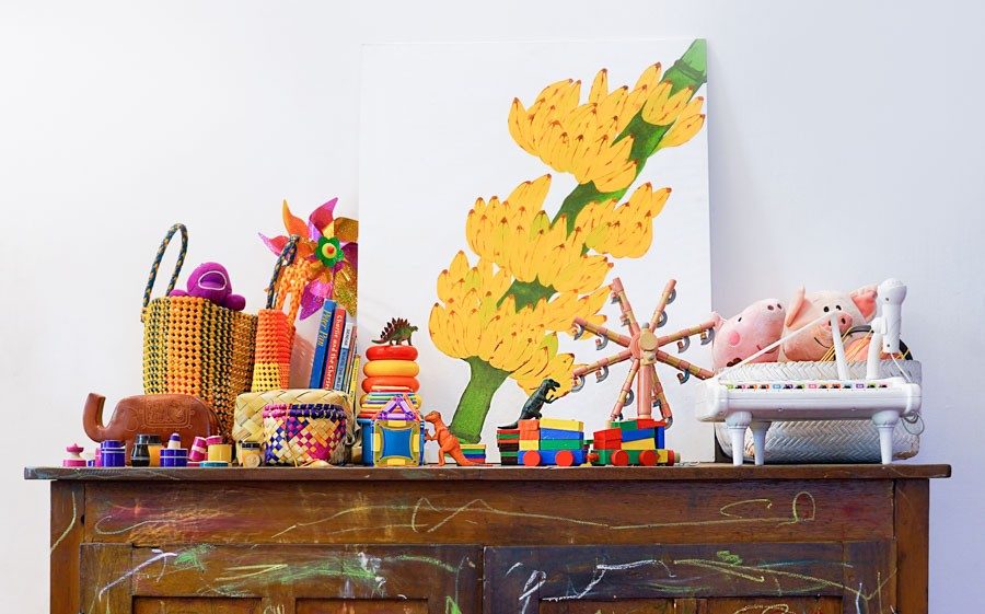 A vintage wooden cabinet with crayon marks on its surface, and on which there is a painting of a banana plant and some toys - Beautiful Homes