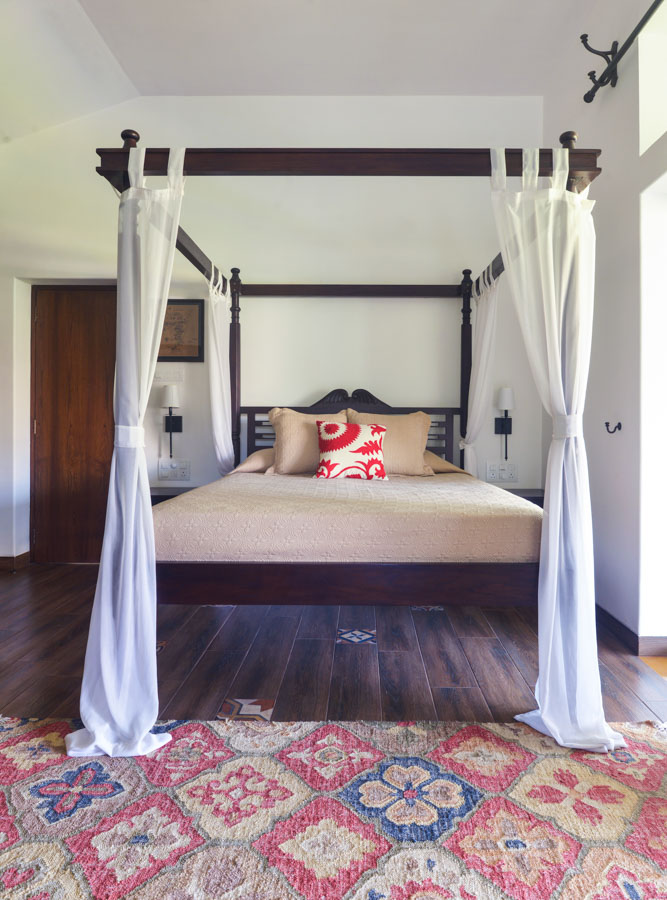 Minimal bedroom décor in Indian bedroom with tiles on a wooden floor, carpet with Indian motifs and one red cushion - Beautiful Homes
