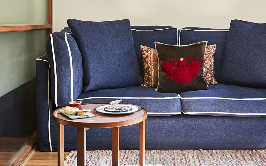Room with a blue sofa, a rug, a coffee table and frames resting on a wooden platform on the wall behind the sofa
