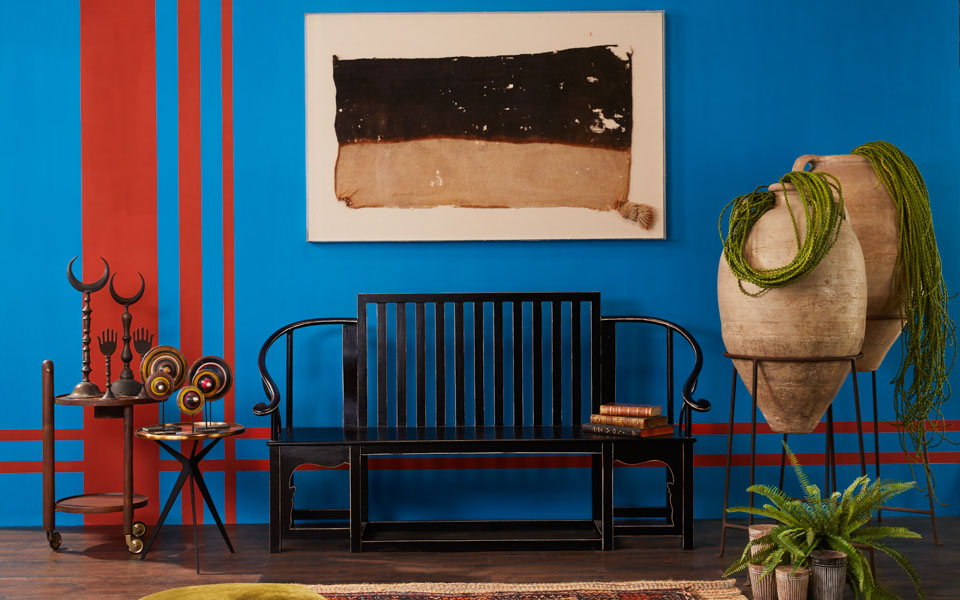  A living room setting with a blue wall with orange stripes on one side, a black bench in front, carpet on the floor, antiques and a frame on a the wall