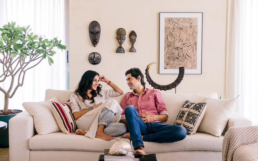 Gaurav and Kirat sitting on their white couch surrounded by souvenirs from their travels on display