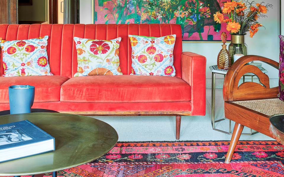 Living room in New Delhi with an red sofa, A large colourful painting on the wall behind, a colourful carpet and a centre table