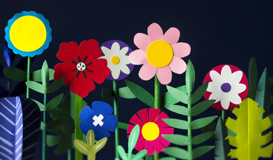 Colourful Paper flowers and green leaves standing in front of a blue background