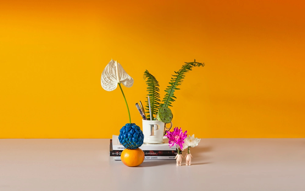 A coffee mug placed on three books, along with two flowers and an orange and a custard apple put together and placed on a table