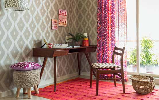 A study area with a wooden table, a cane basket, a window with curtains and Ikat prints