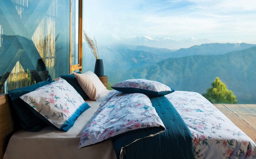 A bed with a floral duvet, pillow covers and a glass beside it with a view of some mountains