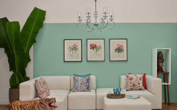 A chandelier hung in a green living room with a white L shaped sofa