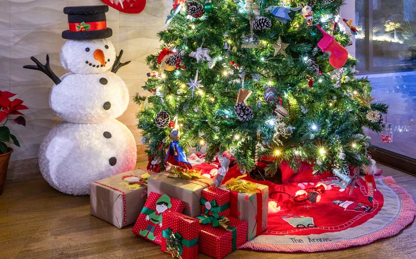 A christmas tree set up in the corner of a room with a snowman beside it and packets of gift below it