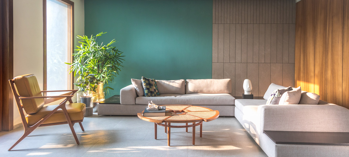 A green living room with a large grey sofa  and a rattan centre table