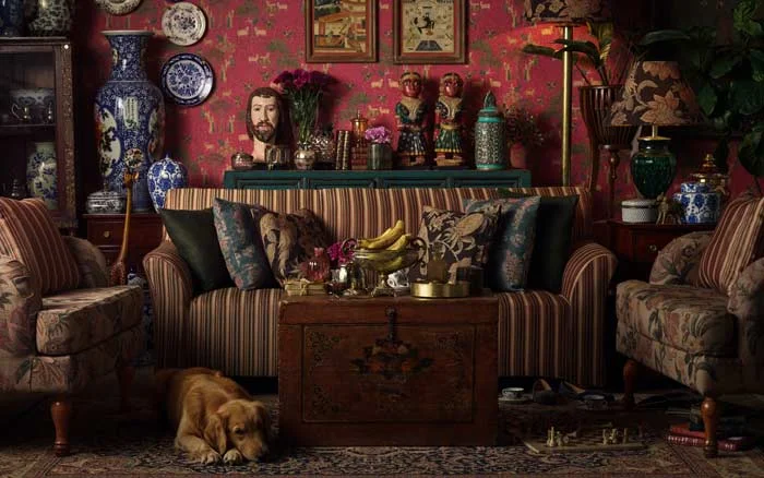 A room with red wallpaper filled with a lot of antiques and and dog lying on a carpet