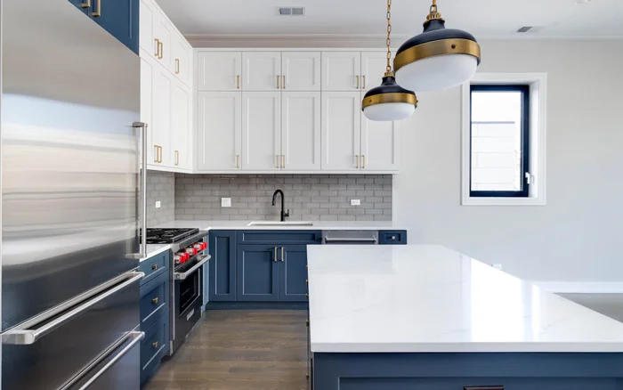 A neat &amp; clean modular kitchen with tiled wall, pendant lights &amp; cabinets of the colour blue &amp; white - Beautiful Homes