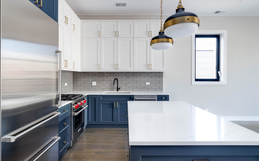 A neat & clean modular kitchen with tiled wall, pendant lights & cabinets of the colour blue & white - Beautiful Homes