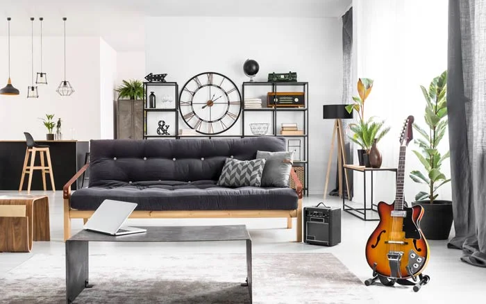 A white living room with a black sofa, a grey rug and a wooden guitar