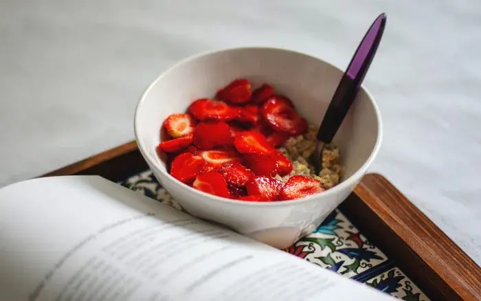 A bowl of Strawberry porridge on a try next to an open book