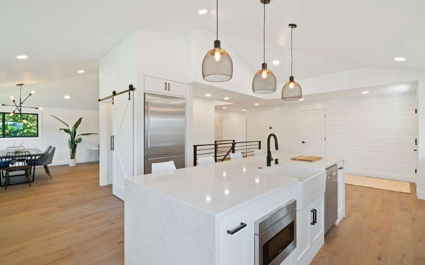 Spacious & all white modular kitchen design with pendant lights & wooden flooring - Beautiful Homes