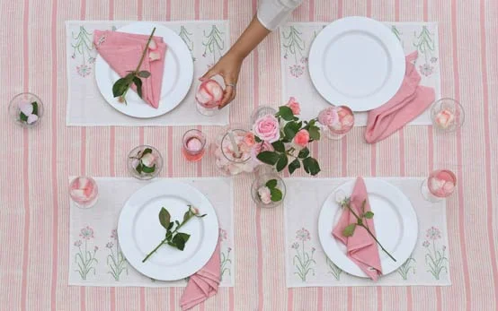 A dining table with a pink table cloth, white plates and pink tissues